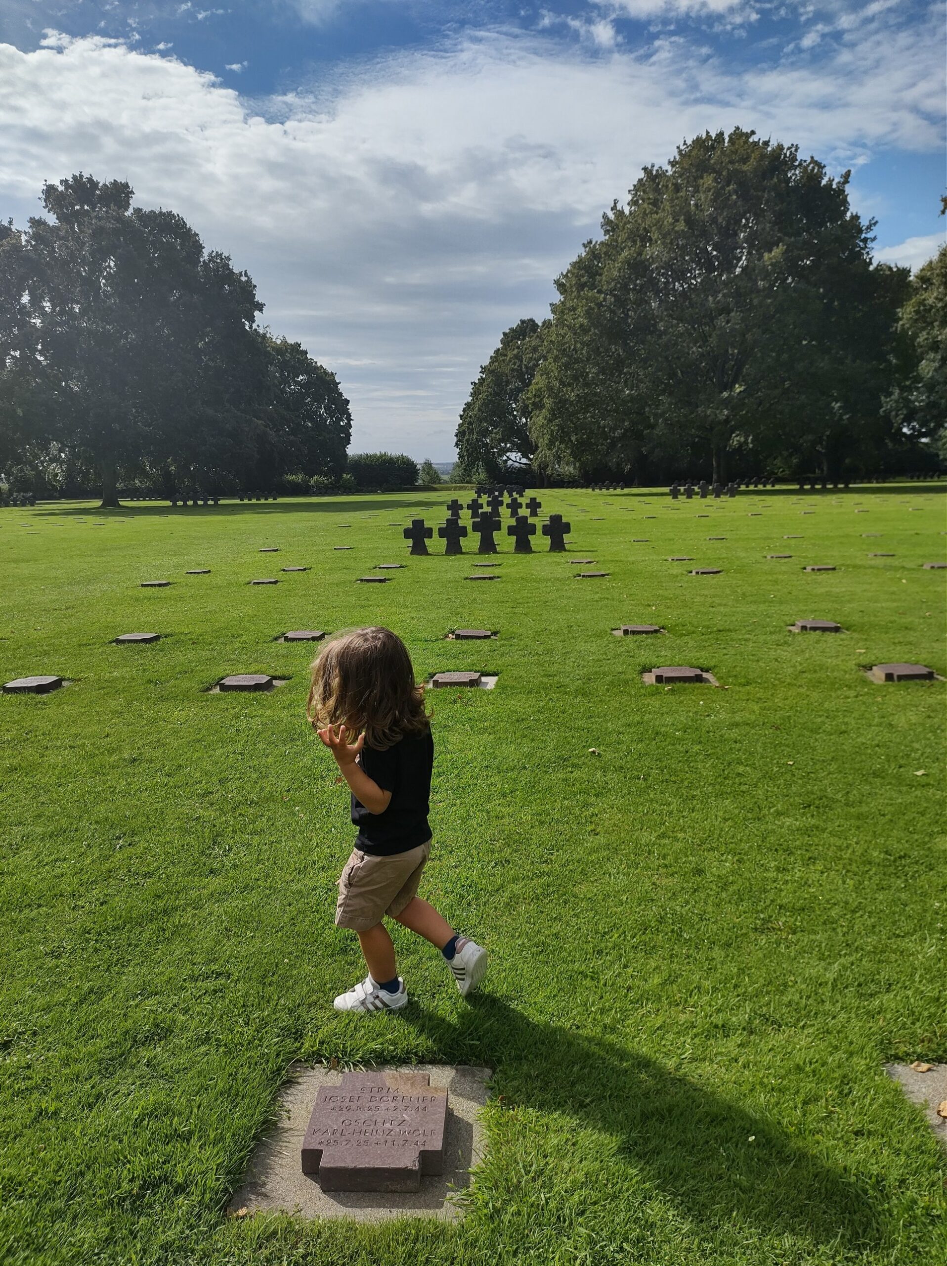 Un bambino cammina tra le lapidi di un grande cimitero sul prato